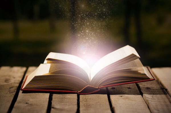 close up of a person holding a light bulb that is glowing and writing in a notebook.