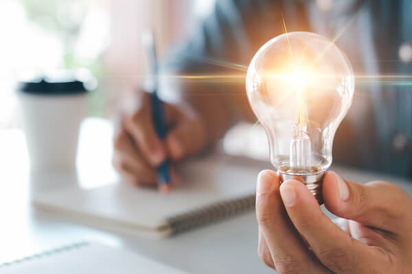 close up of a person holding a light bulb that is glowing and writing in a notebook.