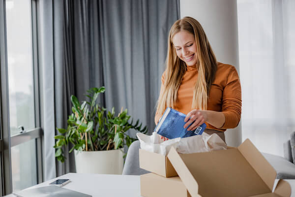 Young woman with long hair feeling happy while opening her online purchase at home. She can't wait to read her new book.