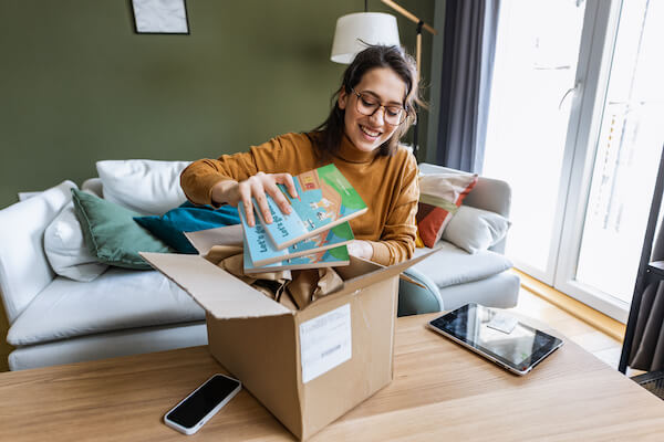 A young woman with brown hair wearing glasses unpacking books she ordered online.